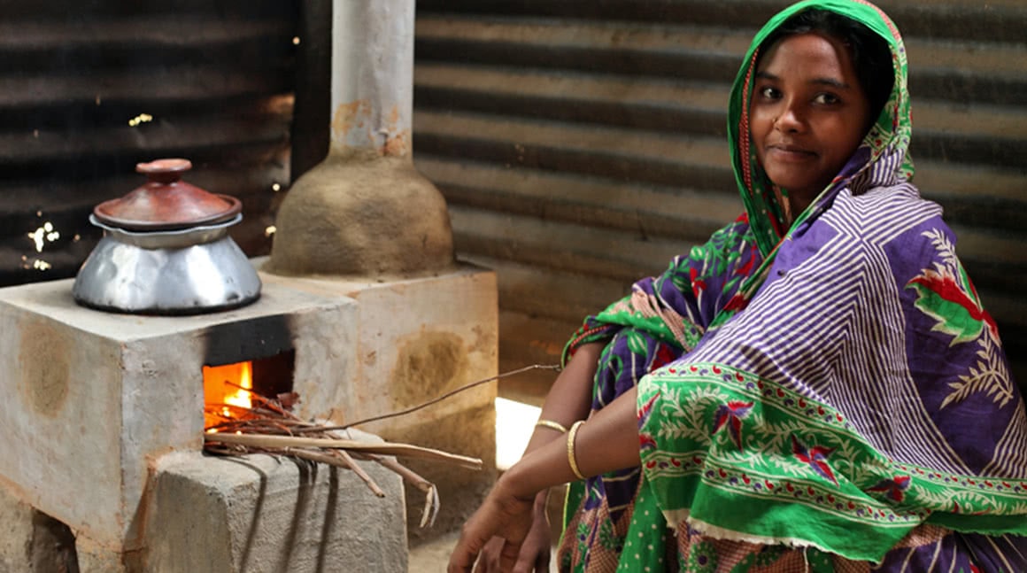 A woman in Bangladesh sits with her Bondhu Chula stove – a clean cooking appliance provided by organisation ClimateCare, who mark-making* support.