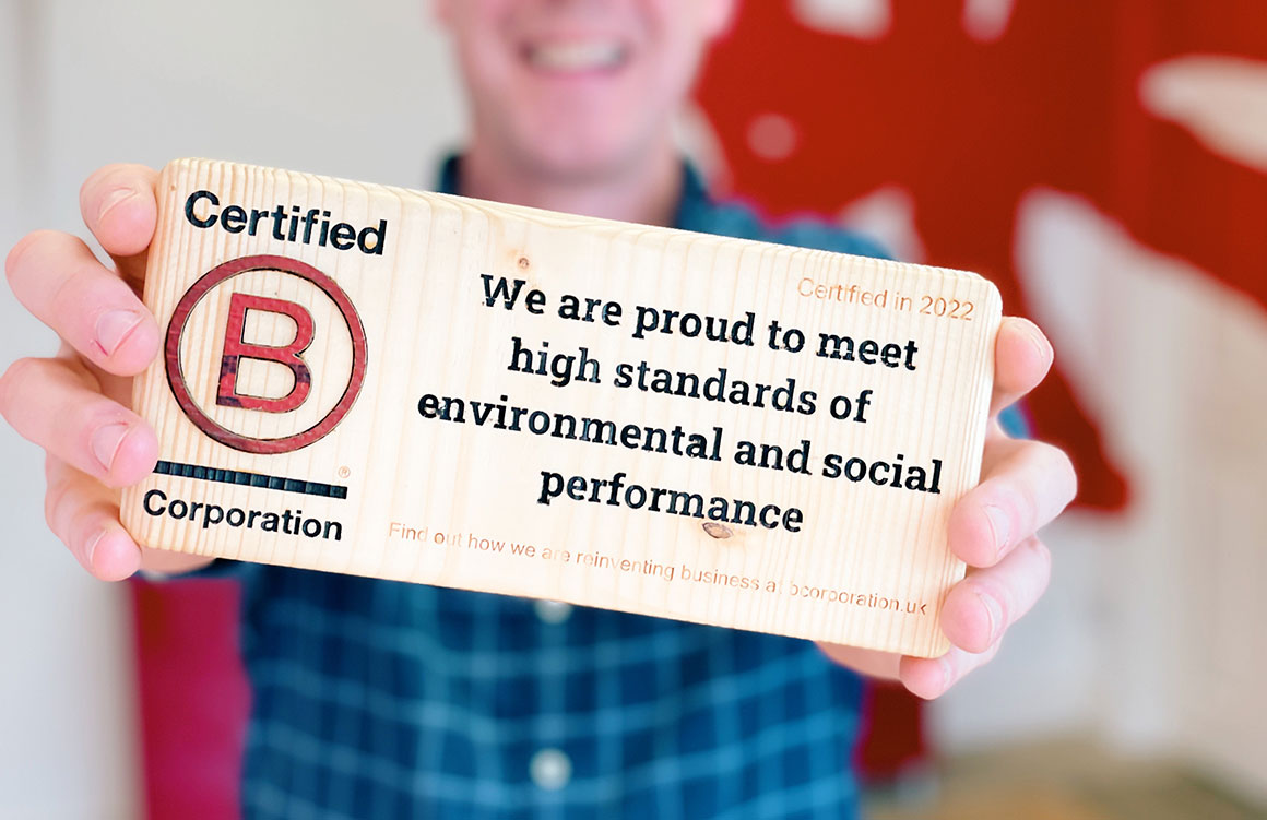 A photo of the author holding B Corp Certification plaque in mark-making*s reception