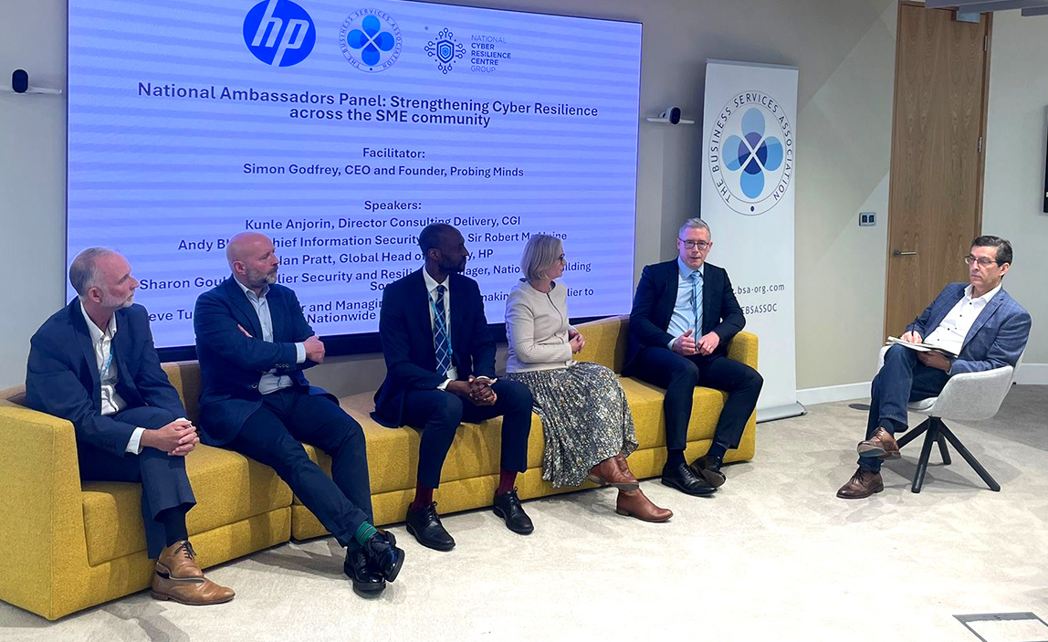 Six panellists seated on yellow modular sofas during the National Ambassadors Panel on Strengthening Cyber Resilience across the SME community. From left to right: Andy Black (Sir Robert McAlpine), Ian Pratt (HP Inc.), Kunle Anjorin (CGI), Sharon Gould (Nationwide Building Society), Steve Turner (mark-making), and Simon Godfrey (Probing Minds, facilitator). A large screen behind them displays the event title and speaker details, with HP, National Cyber Resilience Centre Group, and Business Services Association logos visible. The professional setting features modern office furnishings and branding materials.
